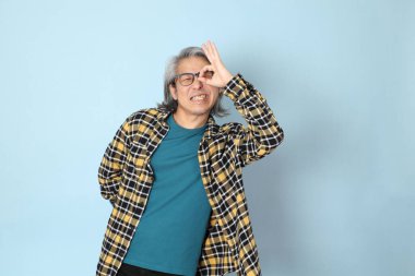 Mavi arka planda duran sarı ekose gömlekli yaşlı Asyalı adam..