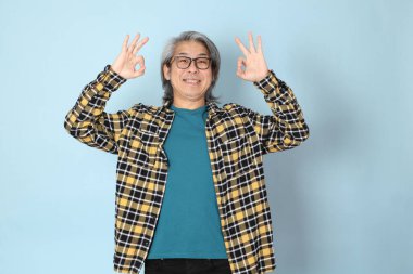 Mavi arka planda duran sarı ekose gömlekli yaşlı Asyalı adam..