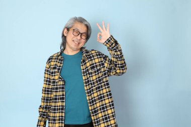 Mavi arka planda duran sarı ekose gömlekli yaşlı Asyalı adam..