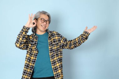 Mavi arka planda duran sarı ekose gömlekli yaşlı Asyalı adam..