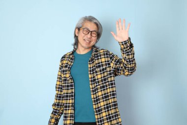 Mavi arka planda duran sarı ekose gömlekli yaşlı Asyalı adam..