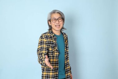 Mavi arka planda duran sarı ekose gömlekli yaşlı Asyalı adam..