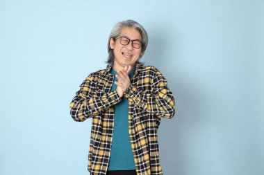 Mavi arka planda duran sarı ekose gömlekli yaşlı Asyalı adam..