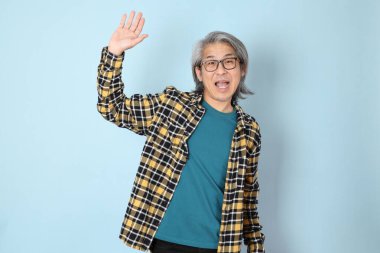 Mavi arka planda duran sarı ekose gömlekli yaşlı Asyalı adam..