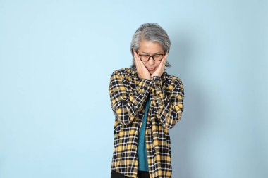 Mavi arka planda duran sarı ekose gömlekli yaşlı Asyalı adam..