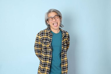 Mavi arka planda duran sarı ekose gömlekli yaşlı Asyalı adam..