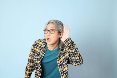 Mavi arka planda duran sarı ekose gömlekli yaşlı Asyalı adam..