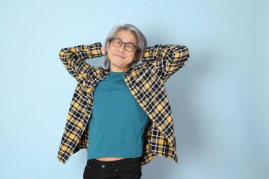 Mavi arka planda duran sarı ekose gömlekli yaşlı Asyalı adam..