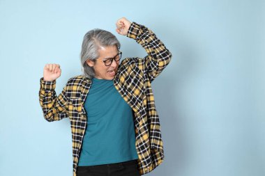 Mavi arka planda duran sarı ekose gömlekli yaşlı Asyalı adam..