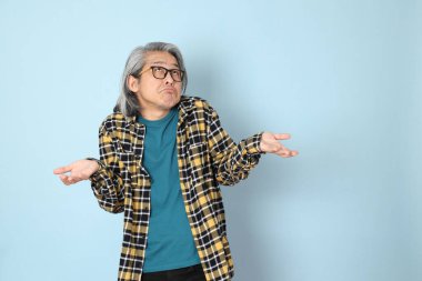 Mavi arka planda duran sarı ekose gömlekli yaşlı Asyalı adam..