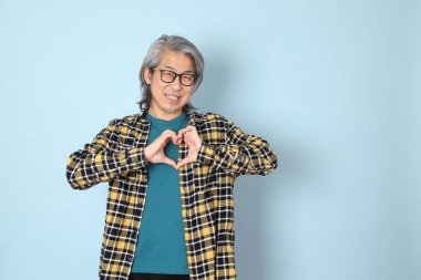 Mavi arka planda duran sarı ekose gömlekli yaşlı Asyalı adam..