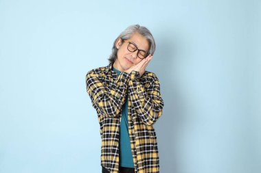 Mavi arka planda duran sarı ekose gömlekli yaşlı Asyalı adam..