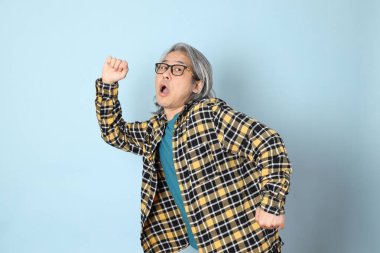 Mavi arka planda duran sarı ekose gömlekli yaşlı Asyalı adam..