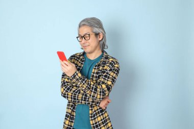 Mavi arka planda duran sarı ekose gömlekli yaşlı Asyalı adam..