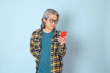 Mavi arka planda duran sarı ekose gömlekli yaşlı Asyalı adam..