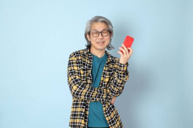 Mavi arka planda duran sarı ekose gömlekli yaşlı Asyalı adam..