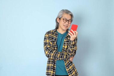 Mavi arka planda duran sarı ekose gömlekli yaşlı Asyalı adam..