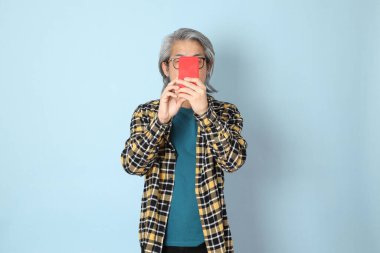 Mavi arka planda duran sarı ekose gömlekli yaşlı Asyalı adam..