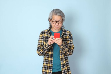 Mavi arka planda duran sarı ekose gömlekli yaşlı Asyalı adam..