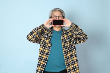 Mavi arka planda duran sarı ekose gömlekli yaşlı Asyalı adam..