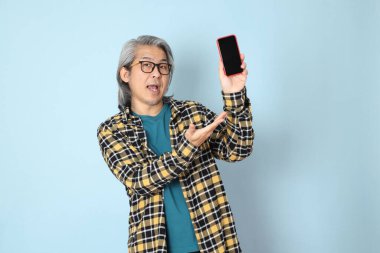 Mavi arka planda duran sarı ekose gömlekli yaşlı Asyalı adam..