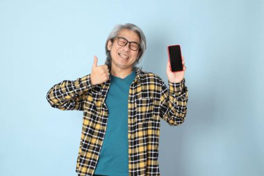 Mavi arka planda duran sarı ekose gömlekli yaşlı Asyalı adam..