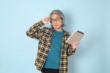 Mavi arka planda duran sarı ekose gömlekli yaşlı Asyalı adam..