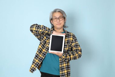 Mavi arka planda duran sarı ekose gömlekli yaşlı Asyalı adam..