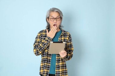 Mavi arka planda duran sarı ekose gömlekli yaşlı Asyalı adam..