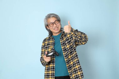 Mavi arka planda duran sarı ekose gömlekli yaşlı Asyalı adam..