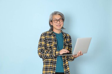 Mavi arka planda duran sarı ekose gömlekli yaşlı Asyalı adam..