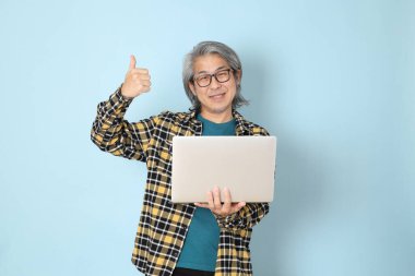 Mavi arka planda duran sarı ekose gömlekli yaşlı Asyalı adam..