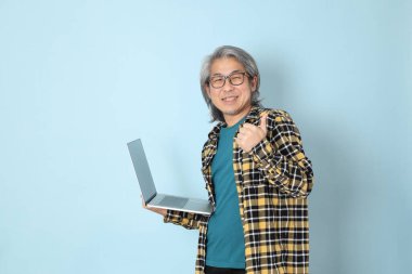 Mavi arka planda duran sarı ekose gömlekli yaşlı Asyalı adam..