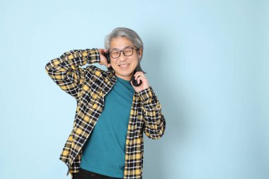 Mavi arka planda duran sarı ekose gömlekli yaşlı Asyalı adam..