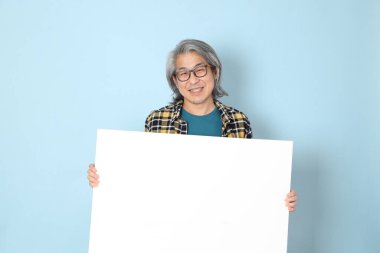 Mavi arka planda duran sarı ekose gömlekli yaşlı Asyalı adam..