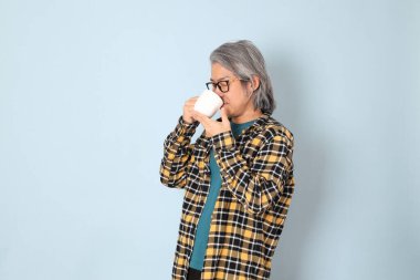 Mavi arka planda duran sarı ekose gömlekli yaşlı Asyalı adam..