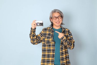 Mavi arka planda duran sarı ekose gömlekli yaşlı Asyalı adam..