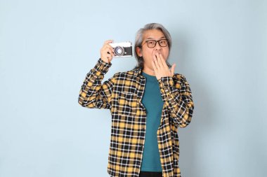 Mavi arka planda duran sarı ekose gömlekli yaşlı Asyalı adam..