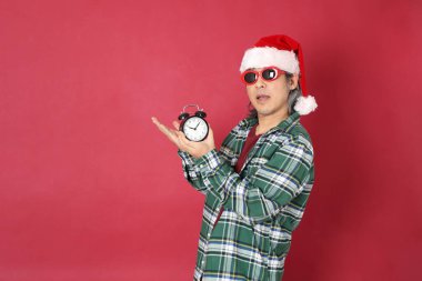 Kıdemli Asyalı adam yeşil ekose gömlek giyiyor ve kırmızı arka planda Noel Baba şapkası var..