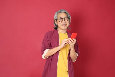 Kırmızı arka planda duran geleneksel Çin kıyafeti giyen kıdemli Asyalı adam..