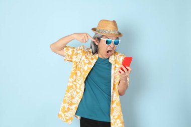 Kıdemli Asyalı yazın giyinen adam mavi arka planda duruyor..