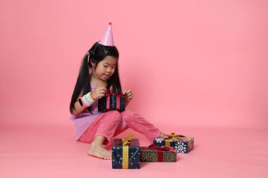 Pembe arka planda hediye kutularıyla oturan genç Asyalı kız..