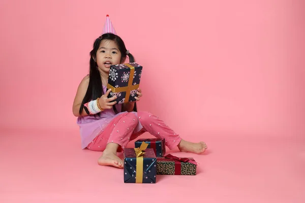 Pembe arka planda hediye kutularıyla oturan genç Asyalı kız..