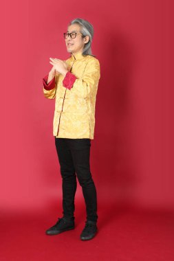 Kırmızı arka planda duran geleneksel altın rengi Çin elbiseleri giyen kıdemli Asyalı adam..