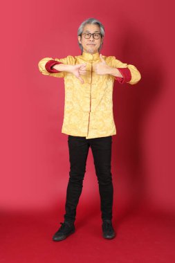 Kırmızı arka planda duran geleneksel altın rengi Çin elbiseleri giyen kıdemli Asyalı adam..