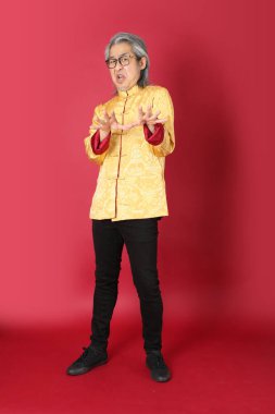 Kırmızı arka planda duran geleneksel altın rengi Çin elbiseleri giyen kıdemli Asyalı adam..