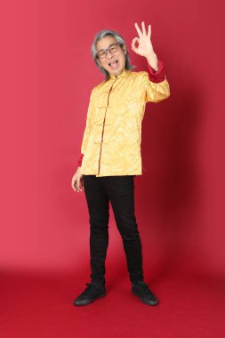 Kırmızı arka planda duran geleneksel altın rengi Çin elbiseleri giyen kıdemli Asyalı adam..