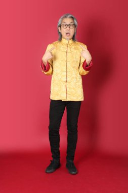 Kırmızı arka planda duran geleneksel altın rengi Çin elbiseleri giyen kıdemli Asyalı adam..