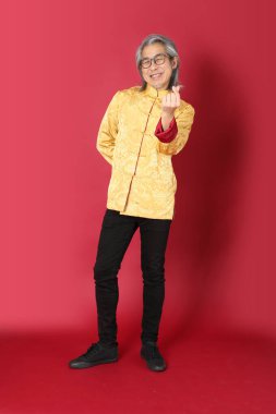 Kırmızı arka planda duran geleneksel altın rengi Çin elbiseleri giyen kıdemli Asyalı adam..