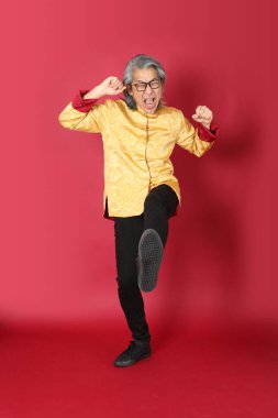 Kırmızı arka planda duran geleneksel altın rengi Çin elbiseleri giyen kıdemli Asyalı adam..